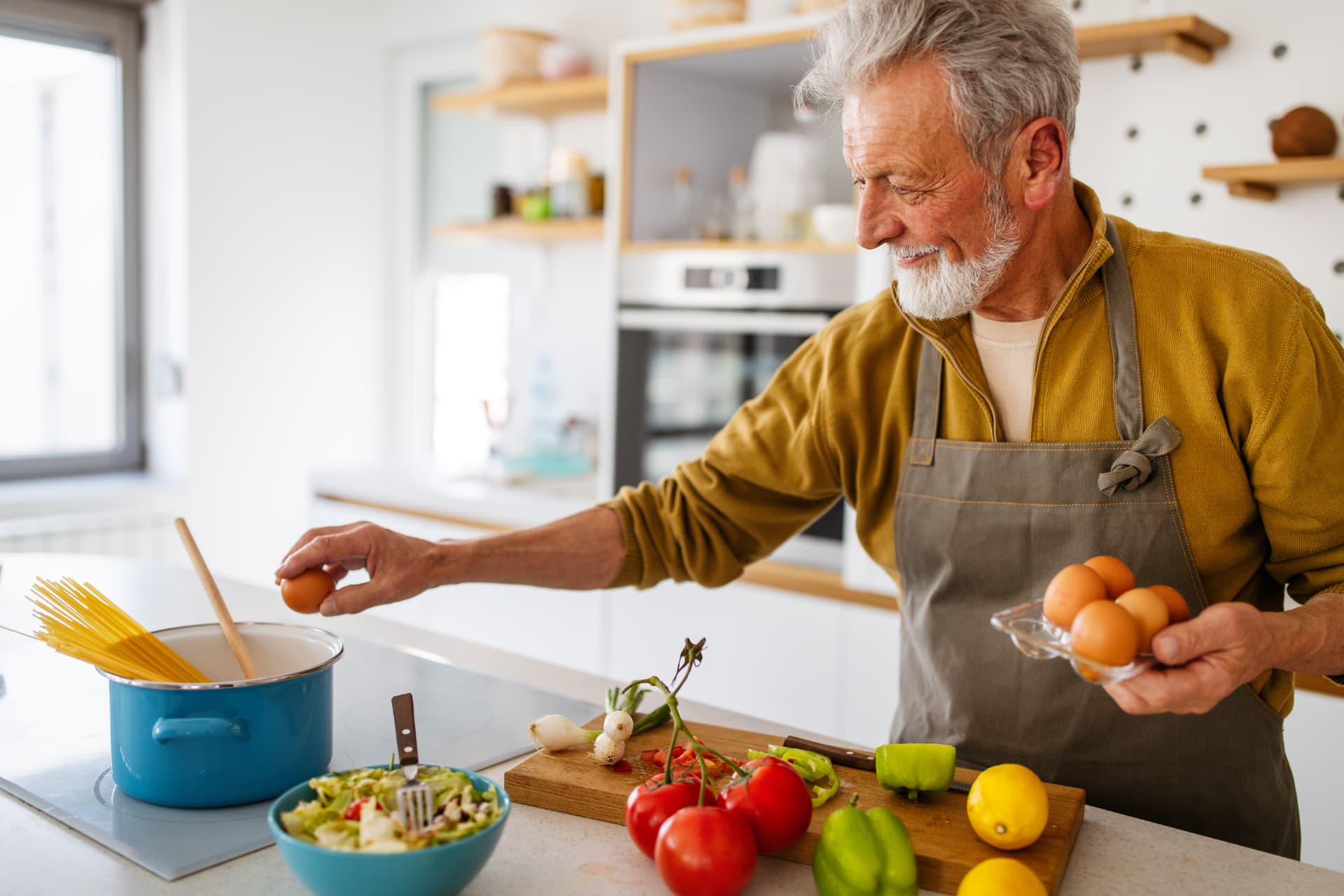 A gray-haired man preparing a meal with fresh vegetables in a bright kitchen